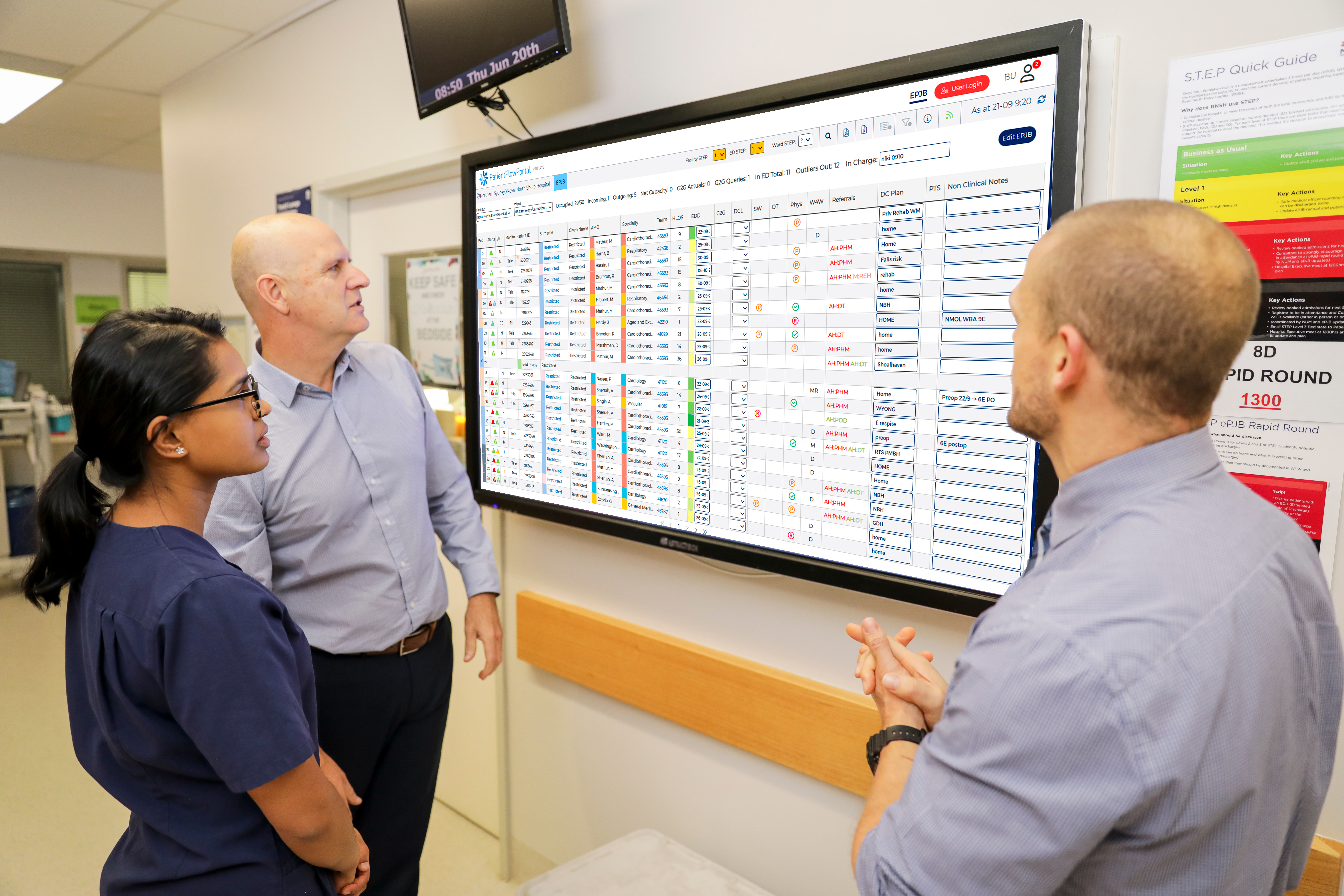Two men and a woman in hospital setting analysing data on a screen.