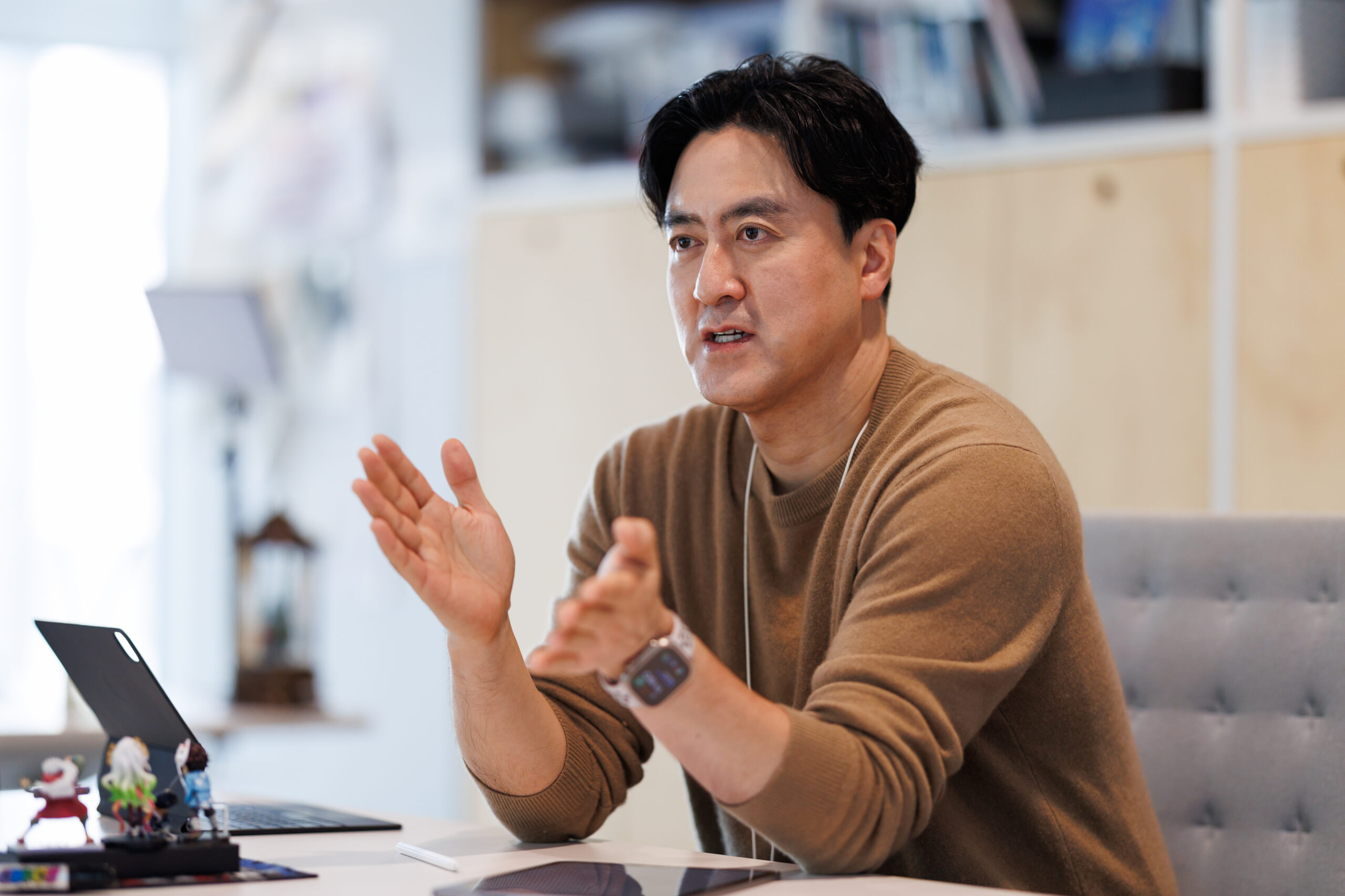 A man in a brown sweater gestures with his hands as he speaks.