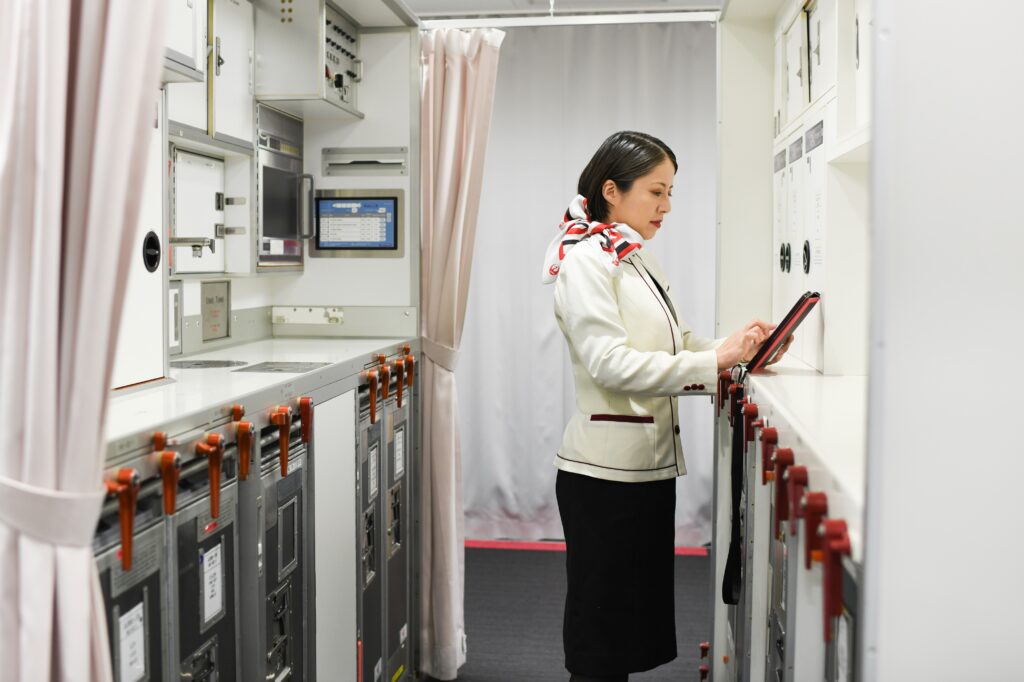 A woman in a flight attendant’s uniform taps on a tablet in an airplane galley.